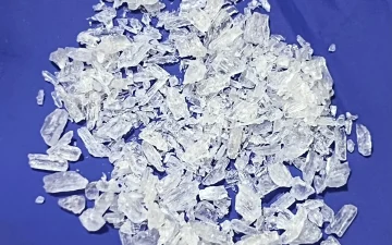 A heap of clear methamphetamine crystal shards of mixed size on a deep blue cloth background