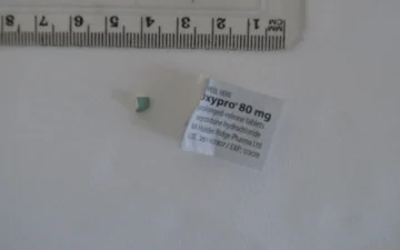 Frammento di compressa di ossicodone accanto all'etichetta di Oxypro 80 mg a rilascio prolungato